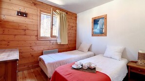 A room with wooden walls, two beds with white linens, a red table with tea cups, and a painting on the wall. - Spacious apartment near slopes with balcony for 8 people (Les Menuires)