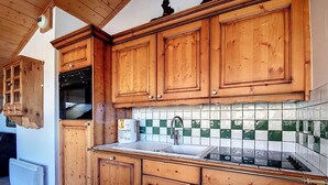 A kitchen with wooden cabinets, a tiled backsplash, and a built-in oven. - Spacious apartment near slopes with balcony for 8 people (Les Menuires)