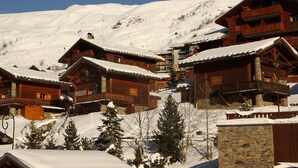 A cluster of wooden cabins with balconies, set against a snowy mountain backdrop. - Spacious apartment near slopes with balcony for 8 people (Les Menuires)