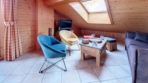A cozy loft-style room with a sloped ceiling, a skylight, a television, a sofa, a coffee table, and two chairs. - Spacious apartment near slopes with balcony for 8 people (Les Menuires)