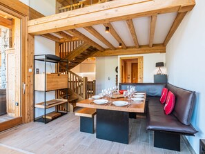 Un coin repas avec une table en bois dressée pour le repas, un banc et un escalier menant à un niveau supérieur.