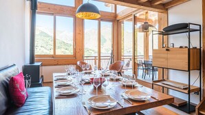 A dining area with a wooden table set for six, large windows offering a mountain view, and a modern pendant light. - Spacious chalet for 10 with sauna and jacuzzi (Saint-Martin-de-Belleville)
