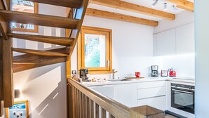 A modern kitchen with white cabinets, a wooden staircase, and a window overlooking the garden. - Spacious chalet for 10 with sauna and jacuzzi (Saint-Martin-de-Belleville)