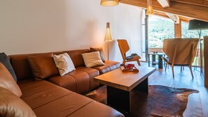 A cozy living room with a brown leather sofa, a wooden coffee table, and a dining area with a chair and table. - Spacious chalet for 10 with sauna and jacuzzi (Saint-Martin-de-Belleville)