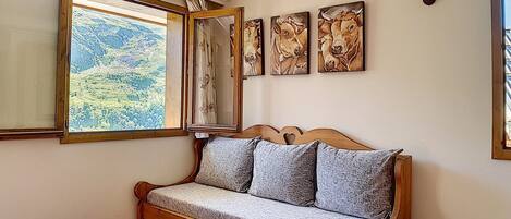Um quarto acolhedor com um sofá de madeira, uma mesinha com xícaras e uma janela com vista para o verde.