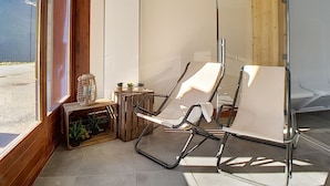 A modern room with two white chairs, a small table with plants, and a view of the outdoors. - Renovated 3-room apartment near slopes, balcony, sauna, steam room, WIFI (Les Menuires)