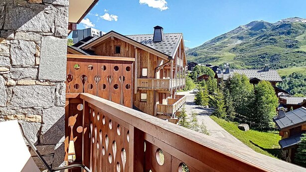 A wooden chalet with a balcony overlooking a mountainous landscape. - Renovated 3-room apartment near slopes, balcony, sauna, steam room, WIFI (Les Menuires)