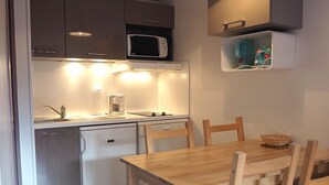 A compact kitchen with a microwave, coffee maker, and a small refrigerator. There is a wooden dining table with chairs. - Renovated 2-room apartment, ski-in/ski-out, southwest balcony (Les Menuires)
