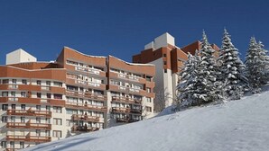 A multi-story hotel with balconies, snow-covered trees, and a clear blue sky. - Renovated 2-room apartment, ski-in/ski-out, southwest balcony (Les Menuires)