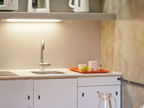 Een moderne keuken met een roestvrijstalen spoelbak, een glazen kan en een aanrecht met een rode dienblad waarop een groene appel en een witte beker staan.