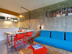 Un espacio habitable moderno con cocina, una mesa de comedor con sillas rojas y un sofá azul.