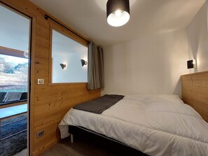 Un dormitorio con cabecera de madera, cama con ropa blanca, ventana con cortinas e iluminación de pared.