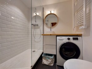 Un baño moderno con ducha compartimentada por vidrio, una lavadora Samsung y un inodoro.