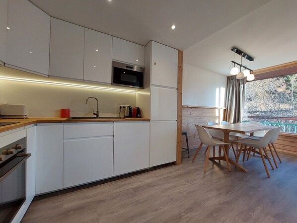 Una cocina moderna con armarios blancos, microondas integrado y una mesa de comedor de madera con sillas.