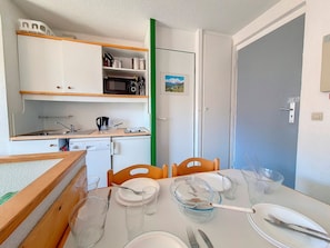 Cozinha compacta com micro-ondas, pia e pequena área de refeições com mesa posta para dois.