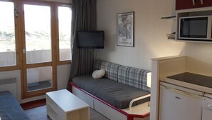 Una habitación compacta con sofá cama, televisión, microondas y una kitchenette pequeña.