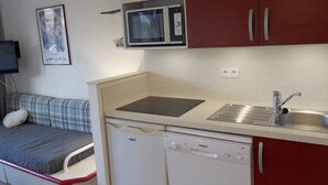 Una kitchenette compacta con microondas, pileta y lavavajillas. Un sofá pequeño se ubica cerca de la cocina.