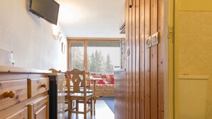 Een houten interieur met een keuken, eethoek en uitzicht op bomen door een raam.