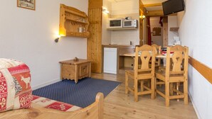 Een gezellige kamer met een houten bed, een klein houten tafeltje, een stoel, een blauw vloerkleed, een houten kast, een magnetron en een televisie.