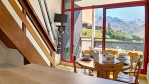 A dining area with a table set for four, a large window with a mountain view, and a staircase with wooden railings. - Bright ski-in/ski-out duplex, 8 pers., 3 bedrooms, Les Menuires (Les Menuires)