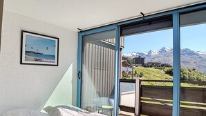 A bedroom with a bed, a glass door leading to a balcony with a mountain view. - Bright ski-in/ski-out duplex, 8 pers., 3 bedrooms, Les Menuires (Les Menuires)