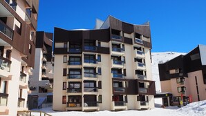 A multi-story hotel with balconies, a ski slope in the background, and a wooden staircase leading to the entrance. - Spacious apartment 6 pers. Near slopes with parking (Les Menuires)