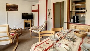 A cozy room with a dining table set for four, a television, and a fireplace. - Spacious apartment 6 pers. Near slopes with parking (Les Menuires)