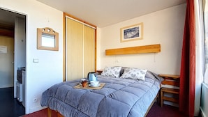 A bedroom with a bed, a bedside table, a nightstand, a window with red curtains, and a picture on the wall. - Cozy apartment for 4 with balcony at ski slopes (Les Menuires)