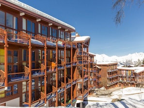 A multi-story hotel with balconies, large windows, and a snowy mountain backdrop.