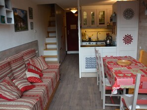 A cozy living room with a sofa and a dining table with chairs. There is a staircase leading to another room.
