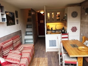 A compact living space with a sofa, a wooden dining table, a kitchen area, and a staircase.