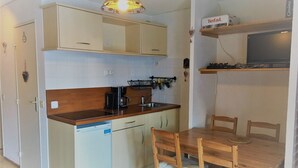 A compact kitchen with a wooden countertop, a coffee maker, and a sink. There is a dining table with chairs and a television on a shelf above it.