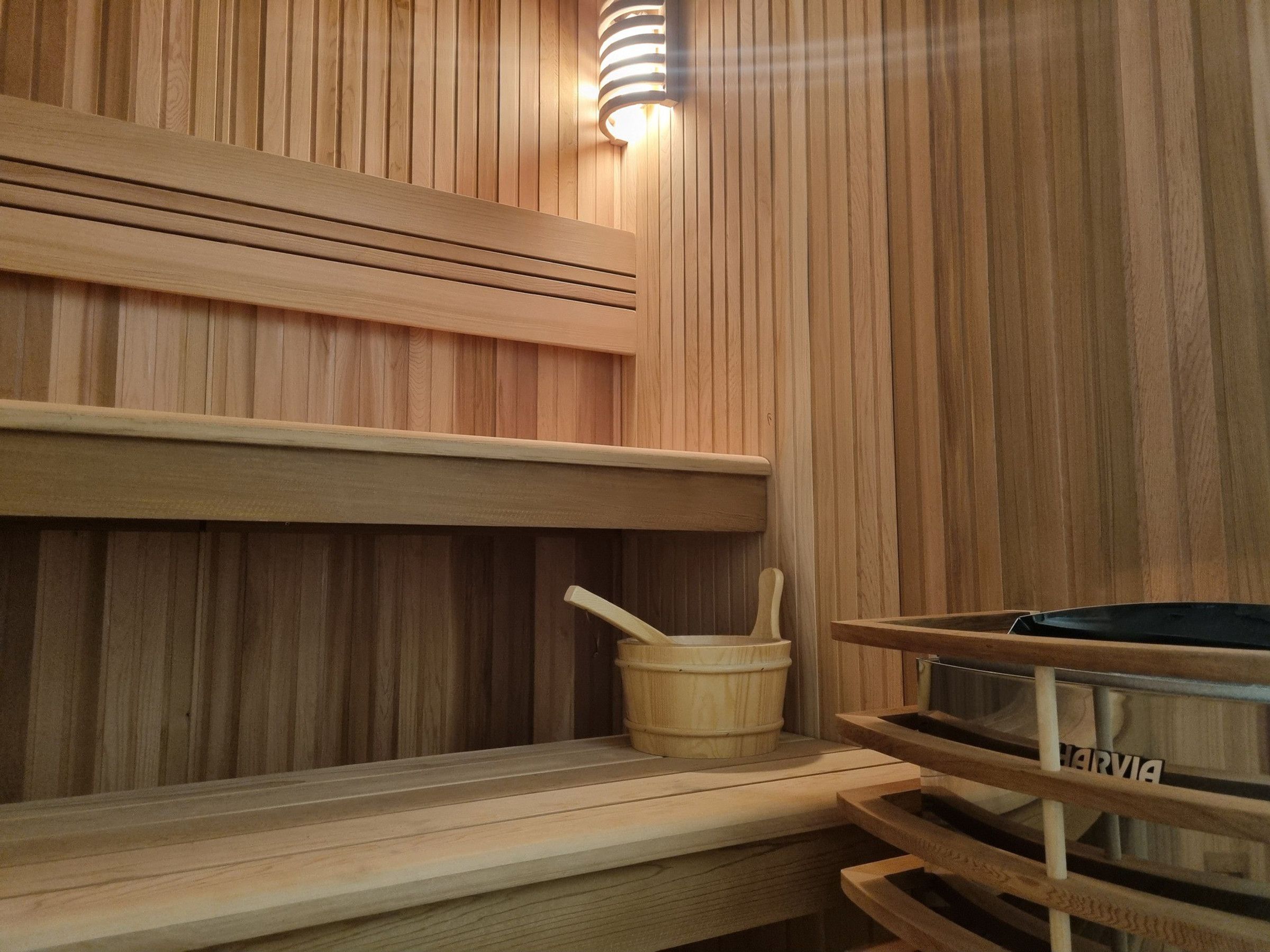 Una sauna de madera con un banco, un balde y una placa con el nombre.