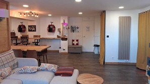 A modern living room with a sofa, a dining table, and a kitchen area in the background. - Spacious renovated apartment in center with balcony - 14p, pets allowed (Plagne Bellecôte)
