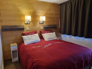 Une pièce aux murs lambrés, comprenant un lit, deux lampes fixées au mur et une fenêtre avec des rideaux.