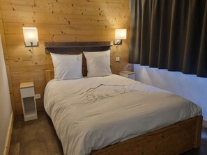 Un lit bien fait, avec une tête de lit en bois, deux tables de chevet et des lampes fixées au mur.