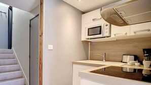 A compact kitchen with a microwave, sink, and stove, adjacent to a staircase leading to another room. - Comfortable duplex 5 pers · Ski-in/Ski-out · Balcony (Les Menuires)