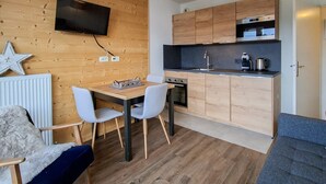 Una cocina compacta con armarios de madera, horno empotrado y televisor de pantalla plana montado en la pared.