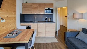 Una cocina compacta con armarios de madera, microondas y cafetera. Hay una mesa de comedor con sillas y un sofá en la sala.