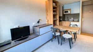 A compact kitchen with a dining area, a TV, and a wooden cabinet with shelves. - Studio cabin at the slopes, pets allowed (Tignes)