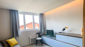 A compact room with a sofa, a small desk, a chair, a television, and a decorative toucan figurine. - Studio cabin at the slopes, pets allowed (Tignes)