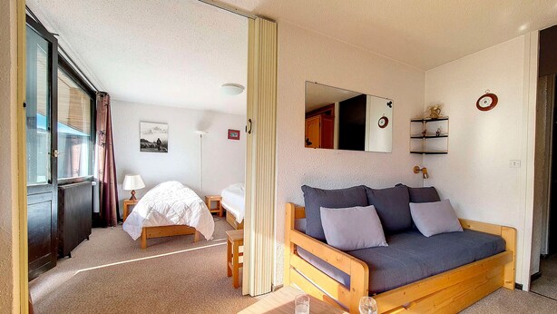 A cozy room with a bed, a sofa, a small table with glasses, and a mirror on the wall. - Bright 2-Room Apartment - Ski-in/Ski-out - Balcony - 6 ppl - Wifi (Les Menuires)