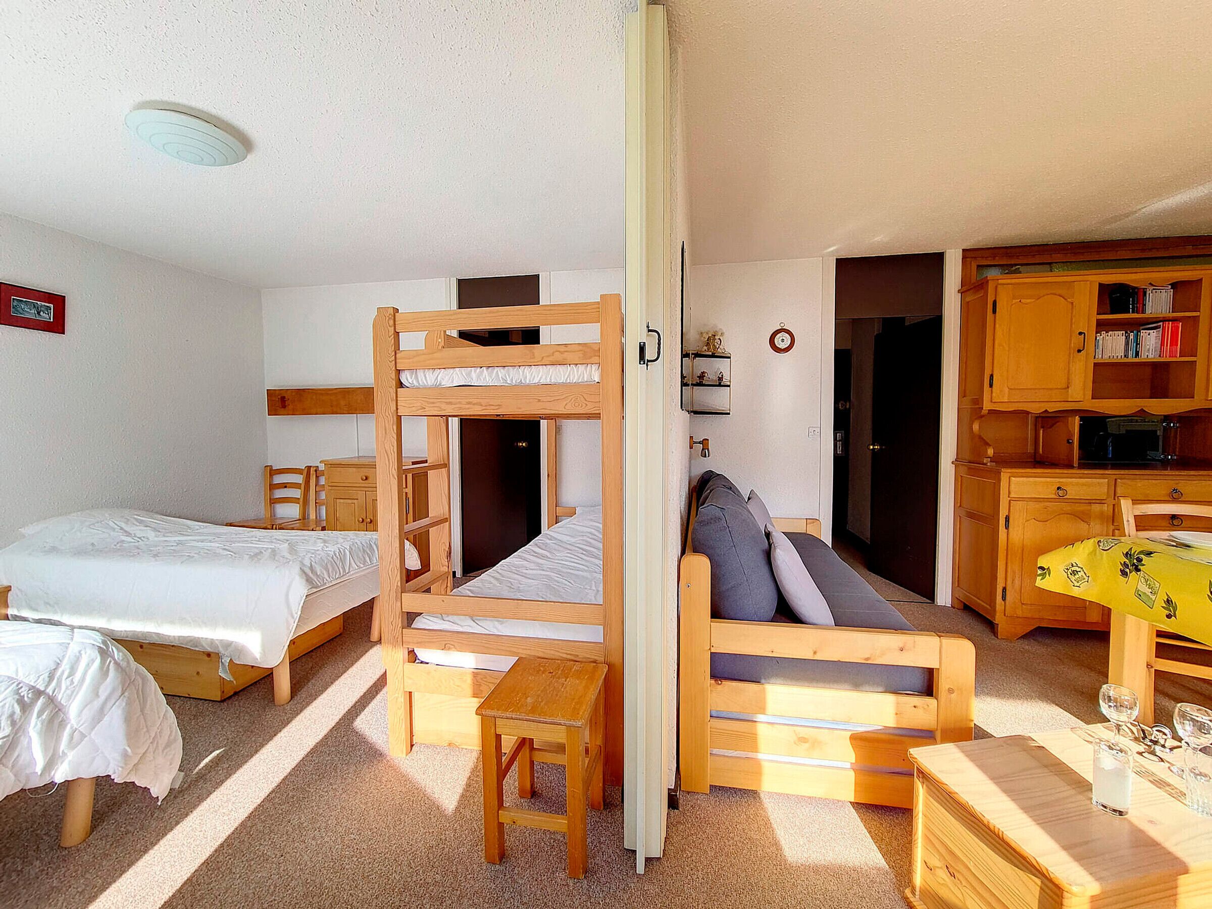 Ein Zimmer mit Etagenbetten, einer Schlafcouch, einem kleinen Tisch und einer Küchenzeile mit Holzschränken.
