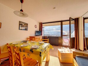 A dining area with a table set for four, a television on a wooden cabinet, and a balcony with a view of the landscape. - Bright 2-Room Apartment - Ski-in/Ski-out - Balcony - 6 ppl - Wifi (Les Menuires)