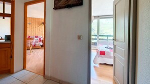 Un couloir mène à une salle à manger avec une table et des chaises, puis à une petite cuisine équipée d’un évier et d’un plan de travail. On peut également admirer, depuis cet espace, un balcon où une table est dressée pour deux personnes.