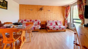 Une pièce chaleureuse avec des murs en bois, une table à manger, deux canapés et une grande fenêtre avec des rideaux.