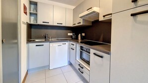 A modern kitchen with white cabinets, a dishwasher, an oven, and a stove. - Bright 3-room apartment near slopes with balcony (Saint-Martin-de-Belleville)
