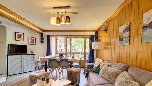 A cozy living room with a sofa, a dining table, and chairs. There is a television on a cabinet, and a window with curtains. - Bright 3-room apartment near slopes with balcony (Saint-Martin-de-Belleville)