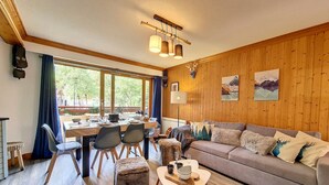 A cozy room with a wooden wall, a sofa, a dining table with chairs, and a small stool. - Bright 3-room apartment near slopes with balcony (Saint-Martin-de-Belleville)