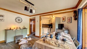 A dining area with a long table set for six, a kitchen in the background, and a clock on the wall. - Bright 3-room apartment near slopes with balcony (Saint-Martin-de-Belleville)